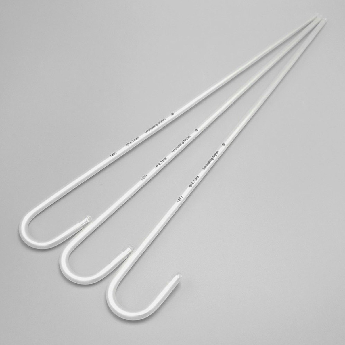 Tre vita plaststavar med krokar i ena änden, liggande på en ljusgrå yta.