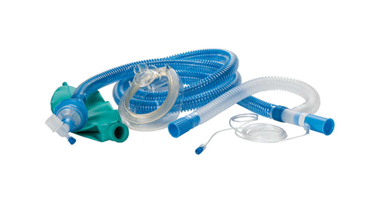 Blått och vitt anestesiandningssystem med mask, slangar och grön andningsblåsa på vit bakgrund.