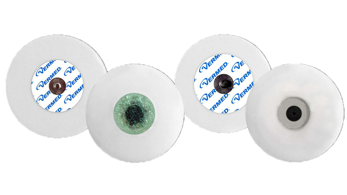 Fyra runda EKG-elektroder av märket Vermed, vita med olika centrumfärger och design.