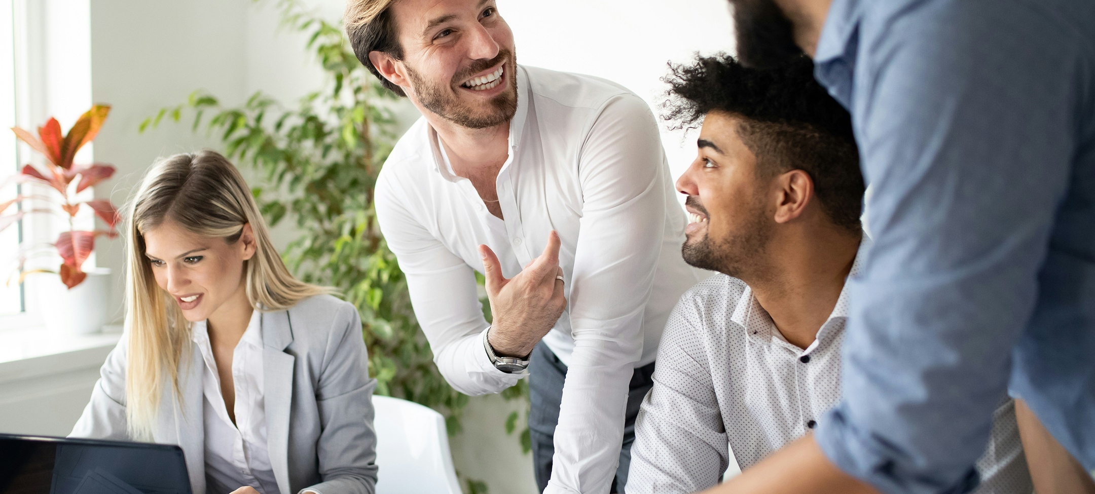Fyra personer har möte på kontor, två män samtalar och en kvinna jobbar vid en laptop.
