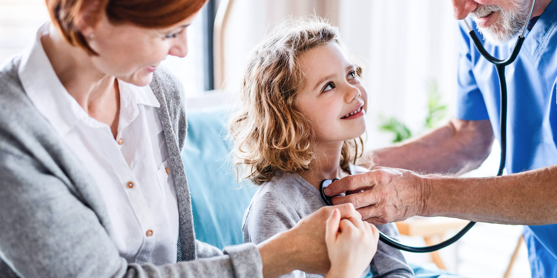 Ung pige, der sidder på sin mors skød under en lægekonsultation, smilende
