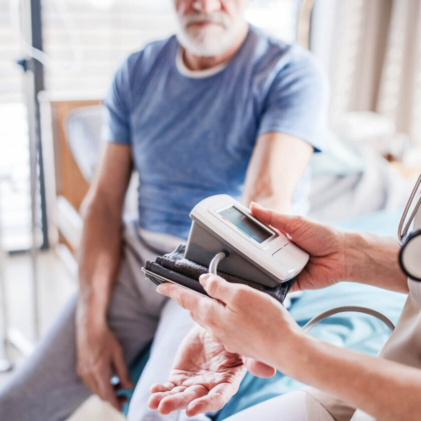 Sjuksköterska mäter blodtryck på äldre man med en digital blodtrycksmätare.