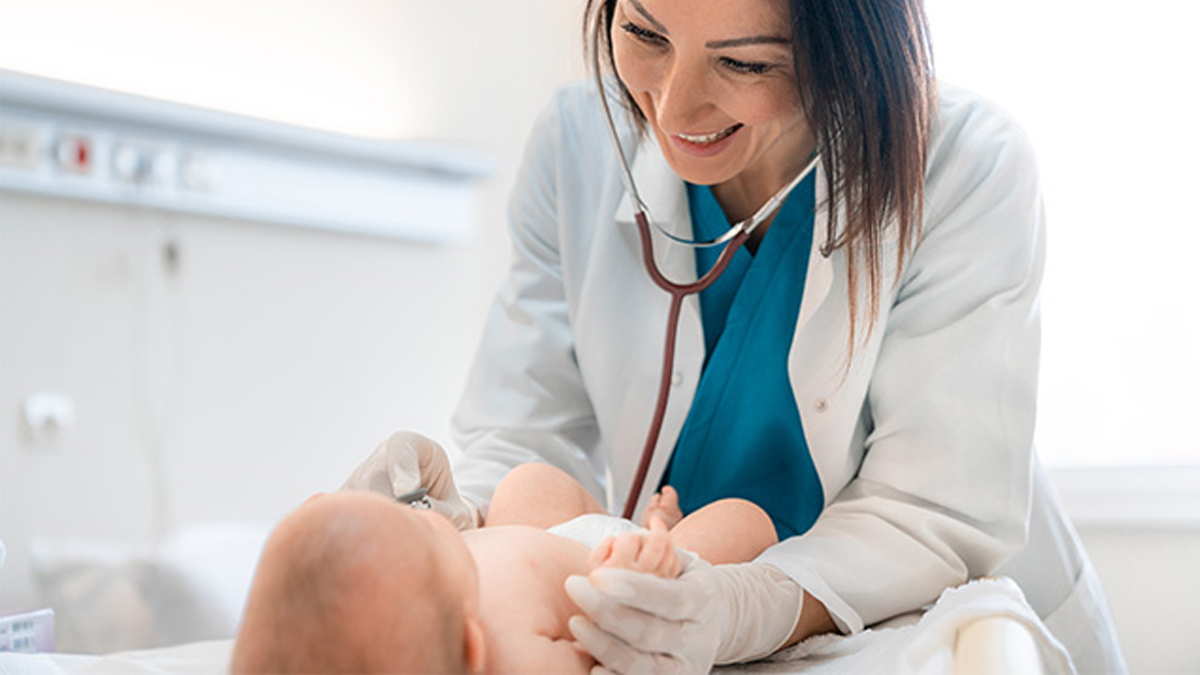 Kvinnlig läkare undersöker en baby med stetoskop, båda ser glada ut på sjukhusrummet.