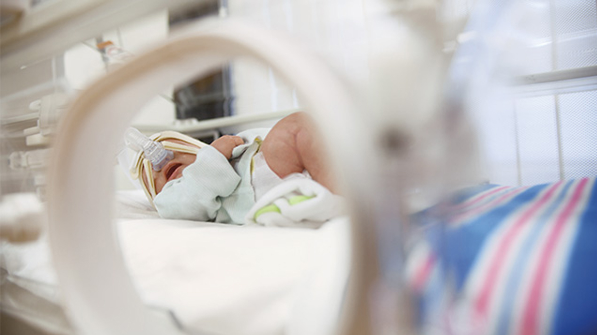 För tidigt född bebis som ligger i en kuvös och bär en andningsmask i en neonatal intensivvårdsavdelning.