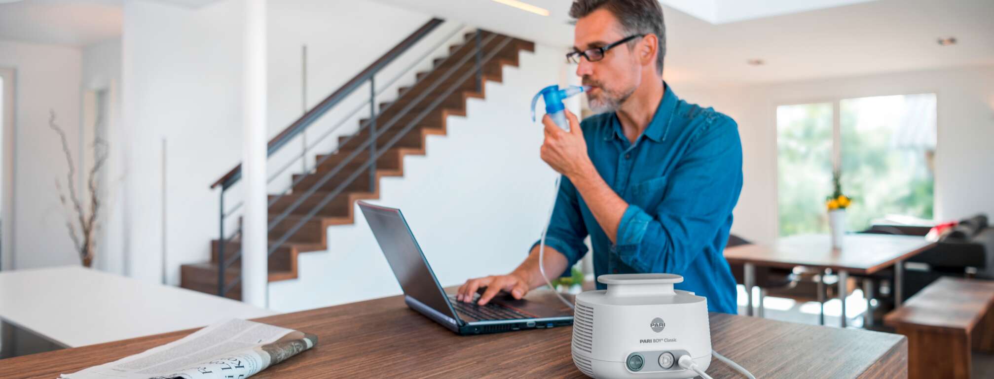 Man-sitting-at-table-with-PC-at-home-getting-inhalation-therapy-with-the-PARI-BOY-Classic