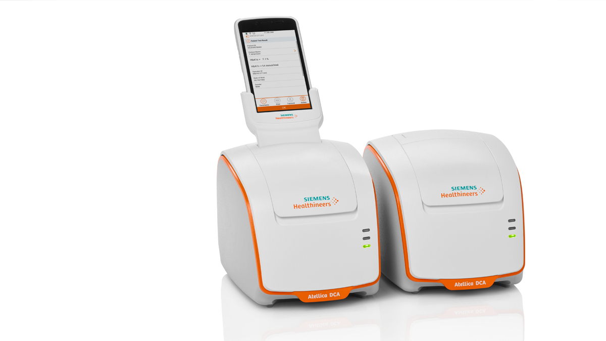 Två vita Siemens Atellica DCA-medicalanalysatorer med orange detaljer, en med display upptill.