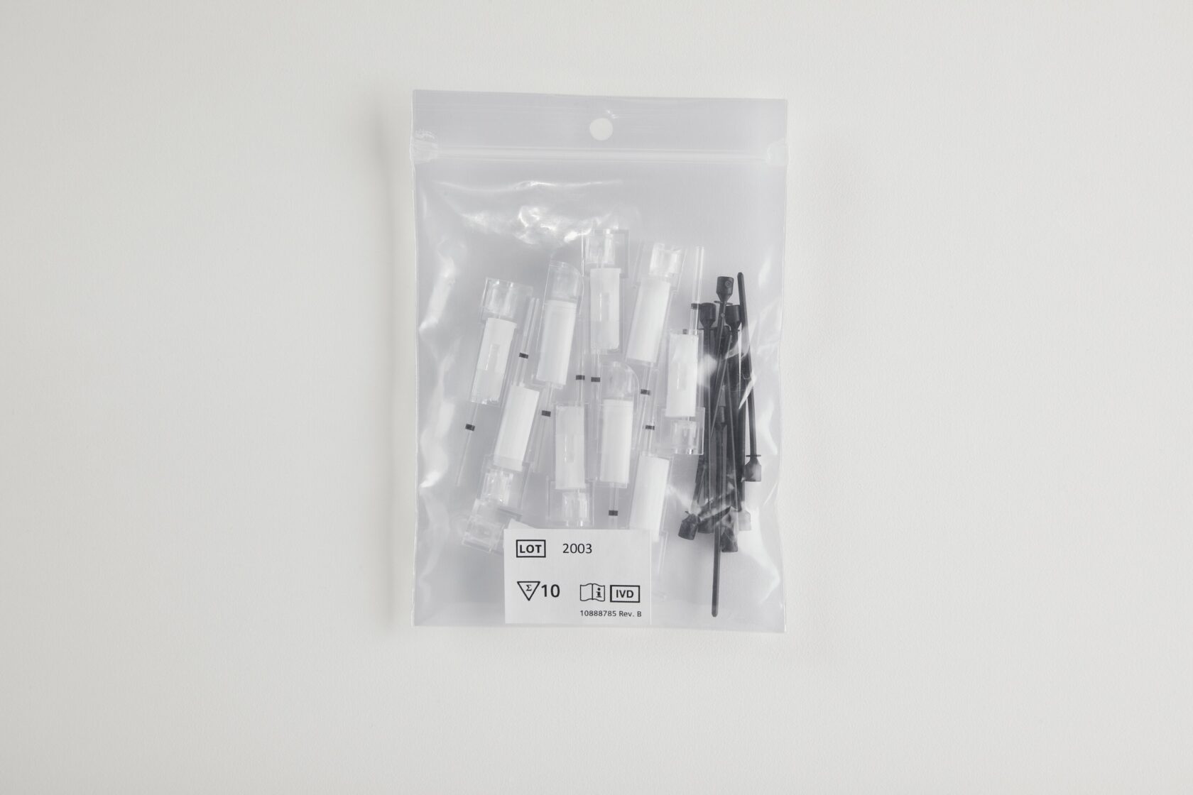 Transparent plastpåse innehållande vita och svarta medicinska eller laboratoriekomponenter på vit bakgrund.