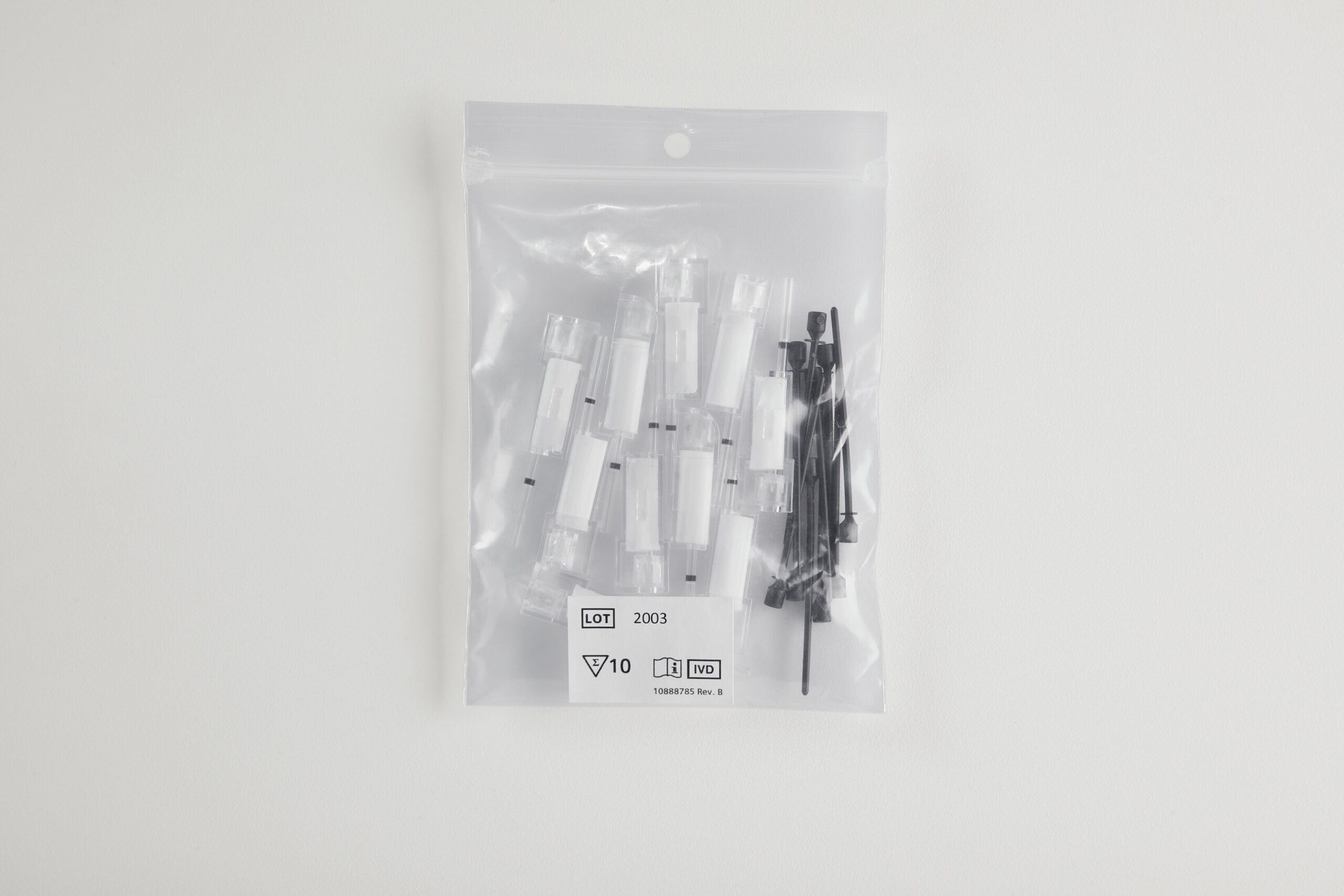 Transparent plastpåse innehållande vita och svarta medicinska eller laboratoriekomponenter på vit bakgrund.